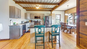 Una cocina amplia con vigas de madera, una isla central, taburetes de bar y un comedor con mesa y sillas de madera.