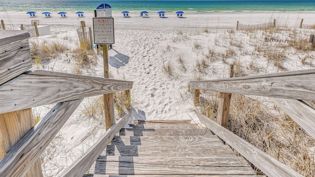 A wooden boardwalk leading to a sandy beach with blue umbrellas. - Waterfront Fort Walton Beach Condo: Pool Access! (Fort Walton Beach)