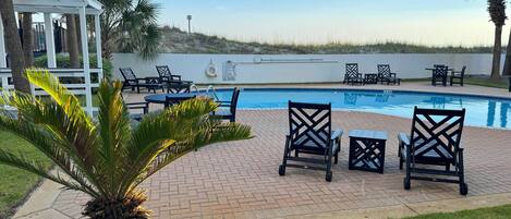 A poolside area with lounge chairs, a pergola, and a view of the beach.