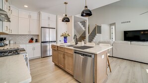 Una cocina moderna con armarios blancos, lavavajillas de acero inoxidable y una isla central con pileta.