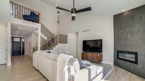 Una sala moderna con un amplio sofá modular, un televisor de pantalla plana, una chimenea y una escalera que sube a un nivel superior.