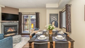 A dining area with a fireplace, a table set for four, and a view to the outside. - Rockies Hideaway - Pool, Waterslide & Hot Tub (Canmore)