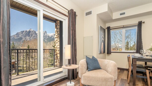 A cozy living room with a sofa, a small table, and a view of mountains through large windows. - Rockies Hideaway - Pool, Waterslide & Hot Tub (Canmore)