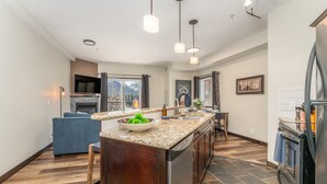 A modern kitchen with a granite countertop, stainless steel appliances, and a view of mountains through the window. - Rockies Hideaway - Pool, Waterslide & Hot Tub (Canmore)