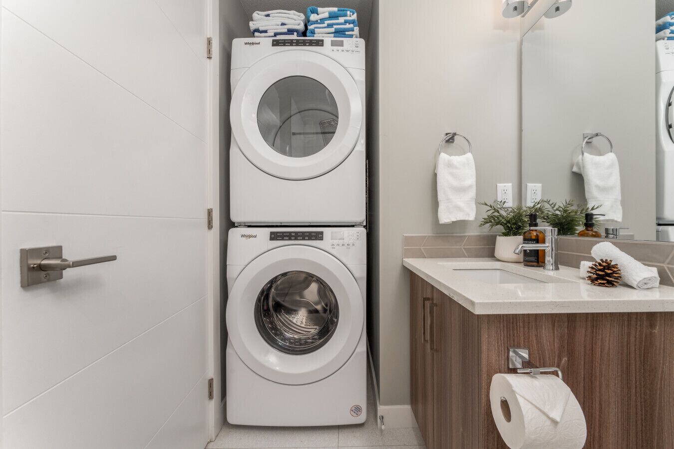 Ein kleines, modernes Badezimmer mit integrierter Waschmaschine und Trockner, einem Holzwaschtisch, einem Spiegel und einer kleinen Pflanze auf der Arbeitsfläche.