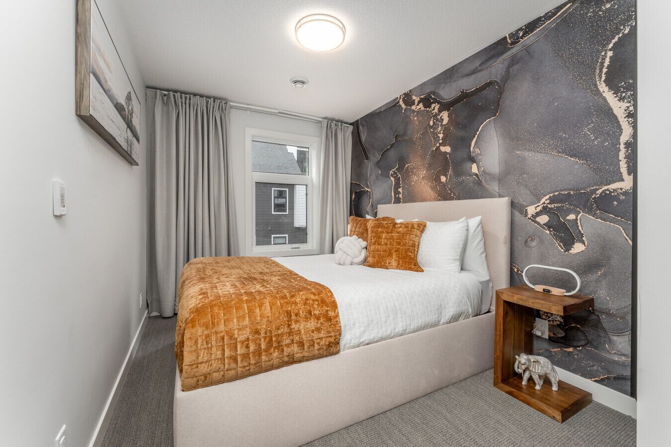 Un dormitorio moderno con una cama grande, una mesita de noche, una lámpara de pared y una ventana con cortinas.