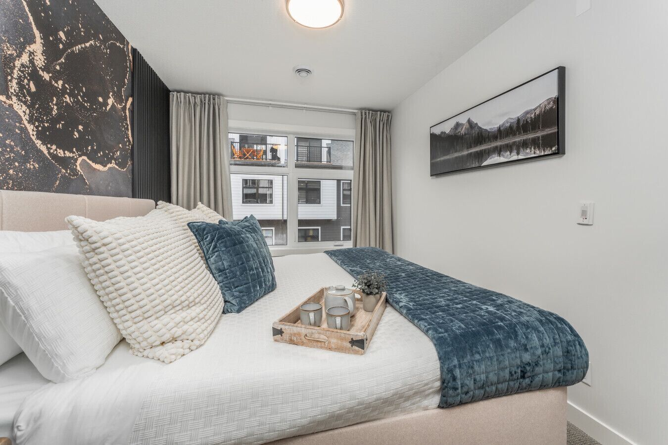 Un dormitorio moderno con una cama grande, vistas a un edificio a través de la ventana, y un cuadro en la pared.