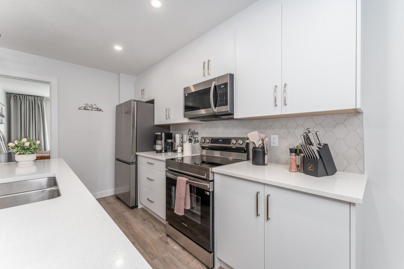 A modern kitchen with white cabinets, stainless steel appliances, and a coffee station.