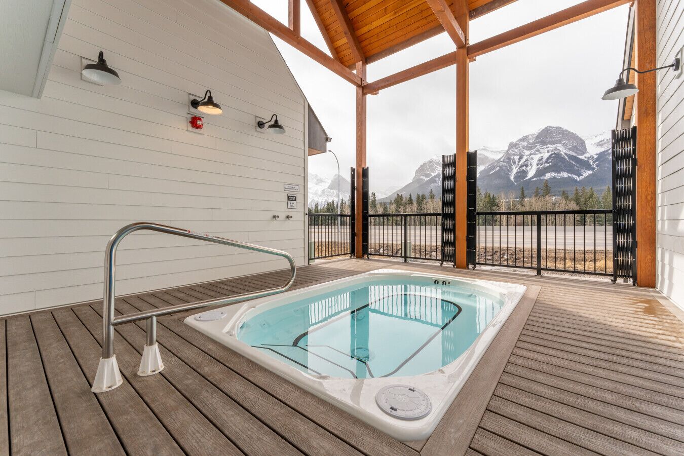 Ein Whirlpool auf einer Holzterrasse mit Blick auf die Berge, Metallgeländern und einem überdachten Bereich mit Holzbalken.