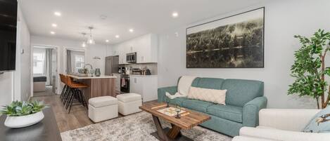 Un salon moderne avec un canapé, une table basse et un coin repas comprenant des chaises, et une cuisine en arrière-plan.