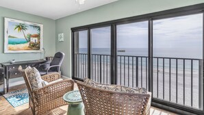 Un balcon avec vue sur la plage, des meubles en osier, un bureau avec une chaise et un ventilateur de plafond.