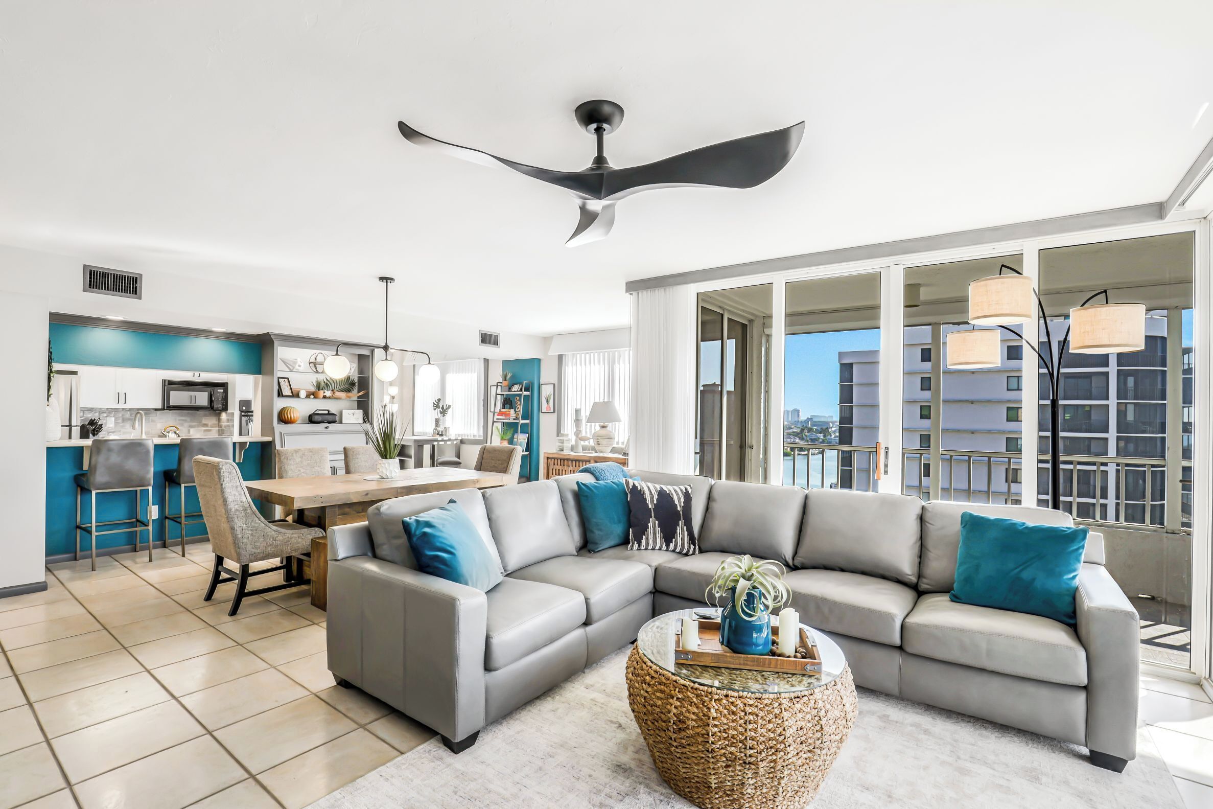 A modern living room with a grey sectional sofa, a dining area with a wooden table, and a kitchen in the background.