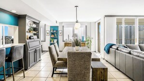 Une cuisine moderne avec un coin repas, comprenant une grande table en bois, des tabourets de bar et un canapé gris.