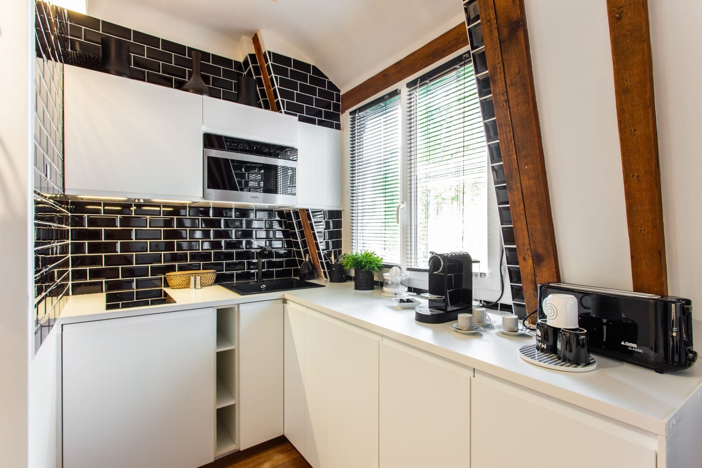 A modern kitchen with white cabinets, black and white tiled backsplash, and a coffee maker on the counter.