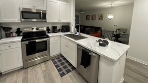 A modern kitchen with white cabinets, stainless steel appliances, a marble countertop, and a black and white rug.