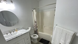 A bathroom with a white sink, toilet, and bathtub. There is a mirror above the sink and a shower curtain with a floral pattern.