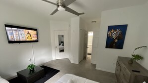 A modern bedroom with a bed, a TV mounted on the wall, a ceiling fan, and a painting on the wall.
