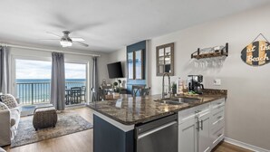 Uma cozinha moderna com bancada de granito, lava-louças embutida e área de refeições com vista para o oceano.