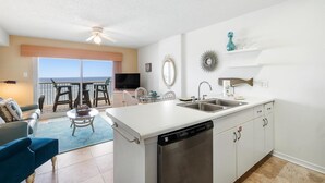 Een moderne keuken met een vaatwasser, een eethoek met een tafel en stoelen, en uitzicht op de oceaan door grote schuifdeuren.