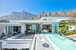 A modern house with a pool, a dining area, and a bedroom with a view of mountains. - Ethereal 4bed Camps Bay Villa Atlantic Reflection (Cape Town)