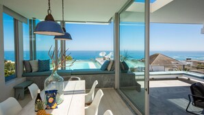 A modern dining area with a view of the ocean, a pool, and a glass-enclosed balcony. - Ethereal 4bed Camps Bay Villa Atlantic Reflection (Cape Town)