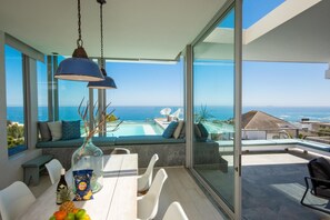 Ein moderner Essbereich mit Blick auf das Meer, einen Pool und einen verglasten Balkon.