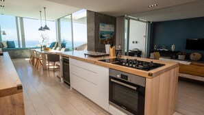 A modern kitchen with a central island, built-in oven, and a dining area with a view of the sea. - Ethereal 4bed Camps Bay Villa Atlantic Reflection (Cape Town)