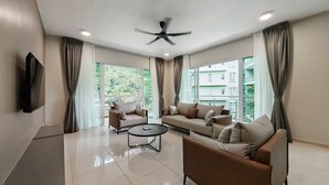 A modern living room with two sofas, a coffee table, and a ceiling fan. Large windows offer a view of a green building. - Mountain & Lake Views' Suite Cycas (Ipoh)