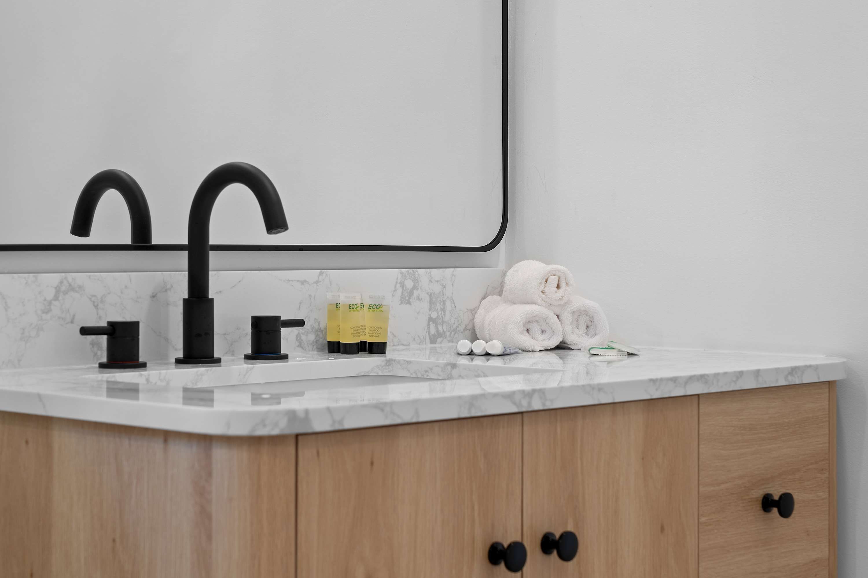 Une salle de bain avec un comptoir en marbre, des robinets noirs et un meuble en bois doté de poignées noires.