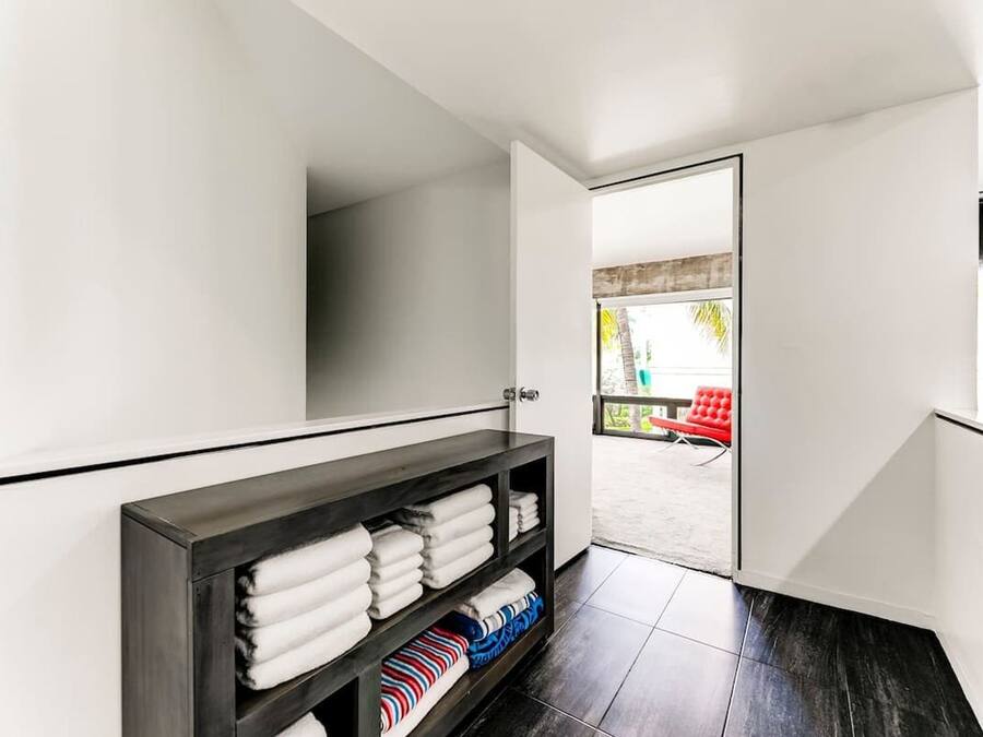 A modern bathroom with a dark wooden vanity, white towels, and a view of an outdoor area with a red chair.