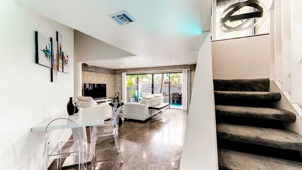 A modern living room with a glass dining table, clear chairs, a sofa, and a staircase. - Entire Townhouse Ft Lauderdale (Fort Lauderdale)
