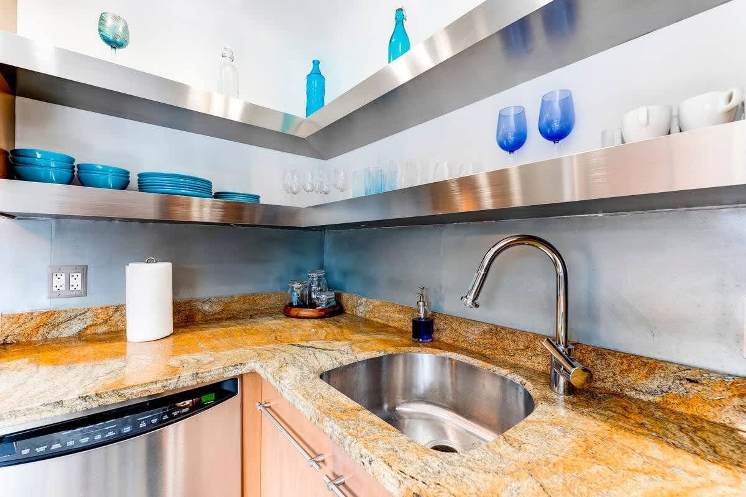 Cozinha moderna com bancada de granito, pia de aço inoxidável e lava-louças embutida.