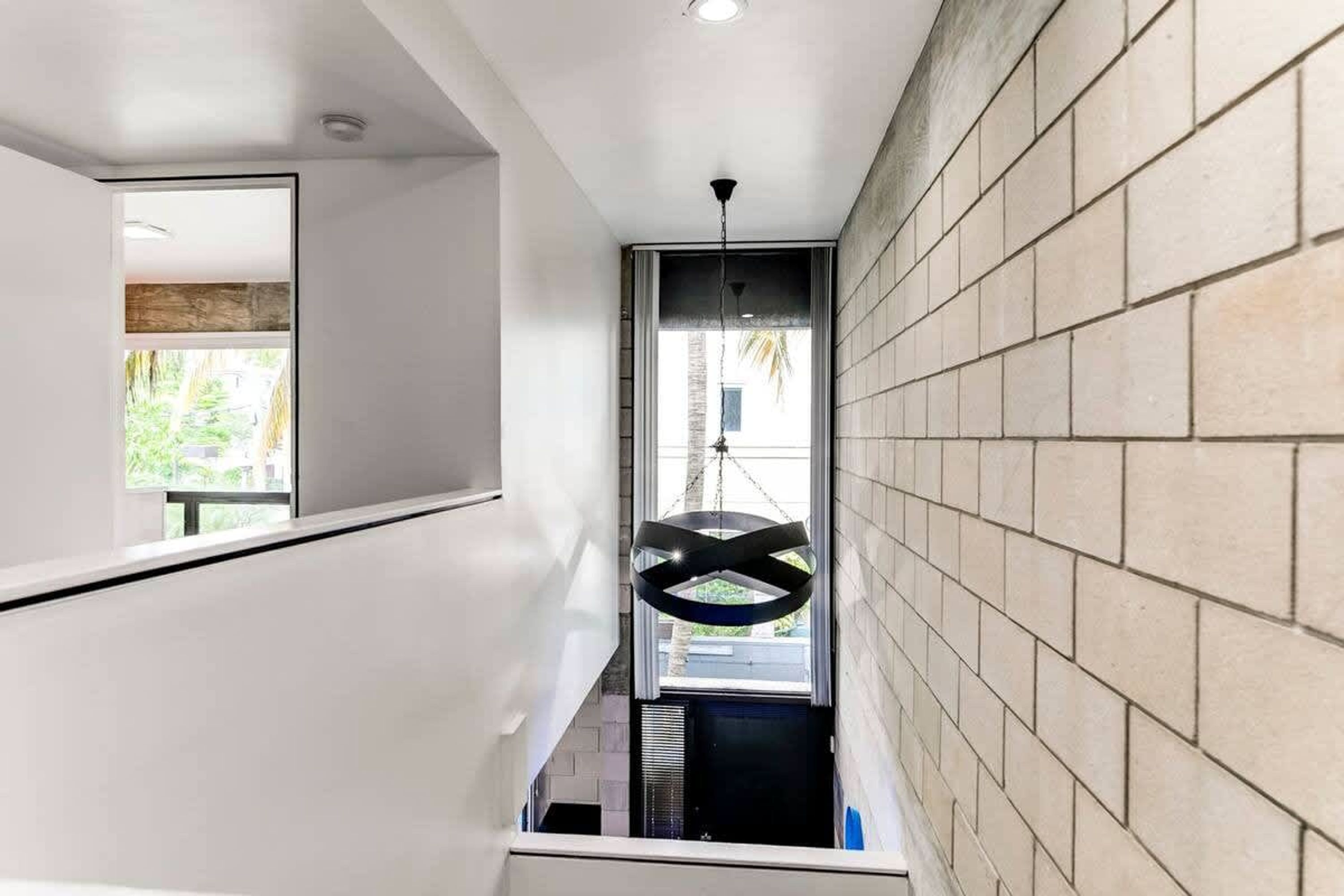 A modern interior with a tiled wall, a hanging light fixture, and a view of the outdoors through a window.