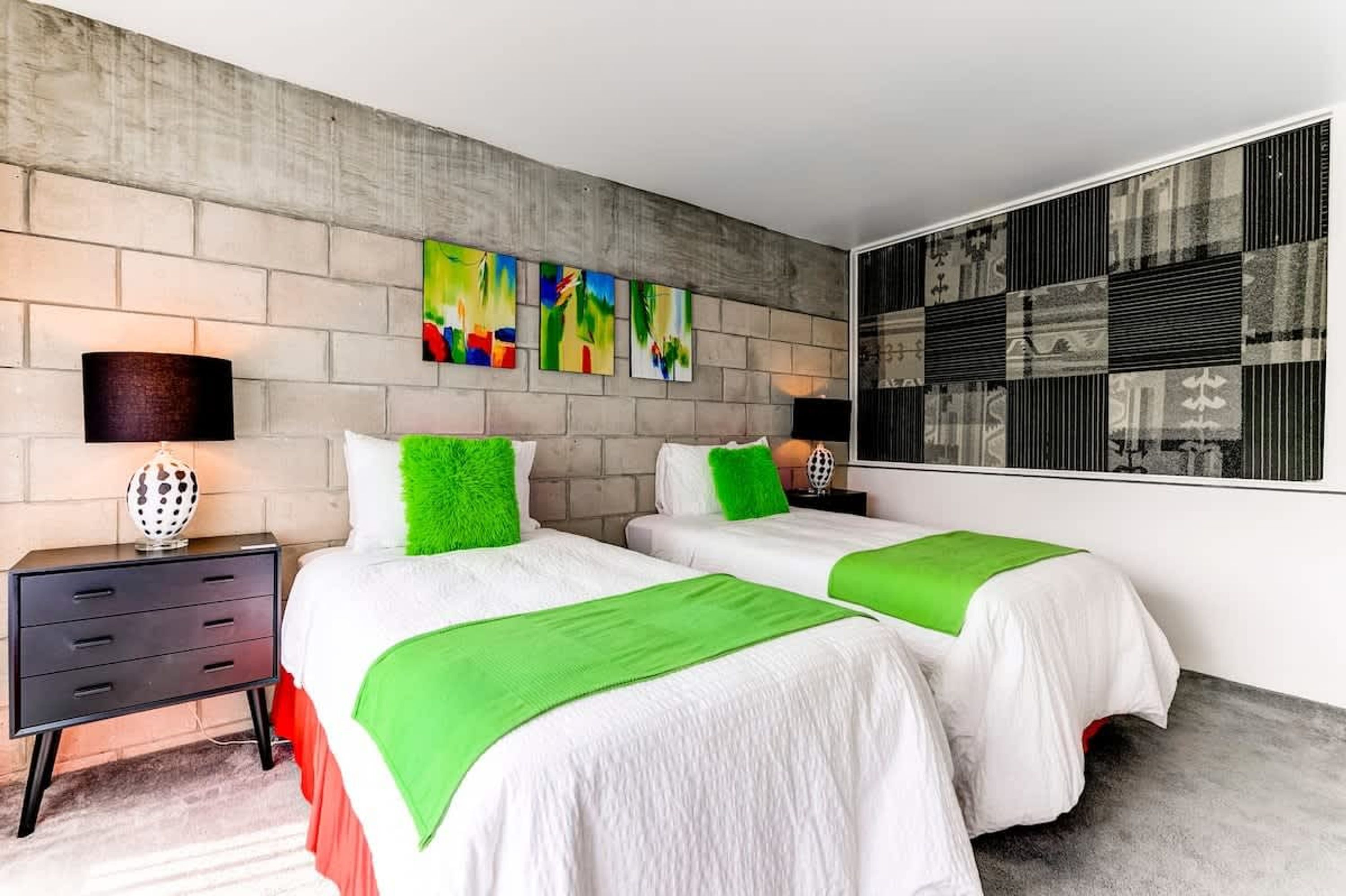 Una habitación de hotel con dos camas, una mesita de noche, una lámpara y obras de arte en las paredes.