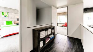 A modern hotel room with a bed, a dark wooden shelf with folded towels, and a view of a red chair outside. - Entire Townhouse Ft Lauderdale (Fort Lauderdale)