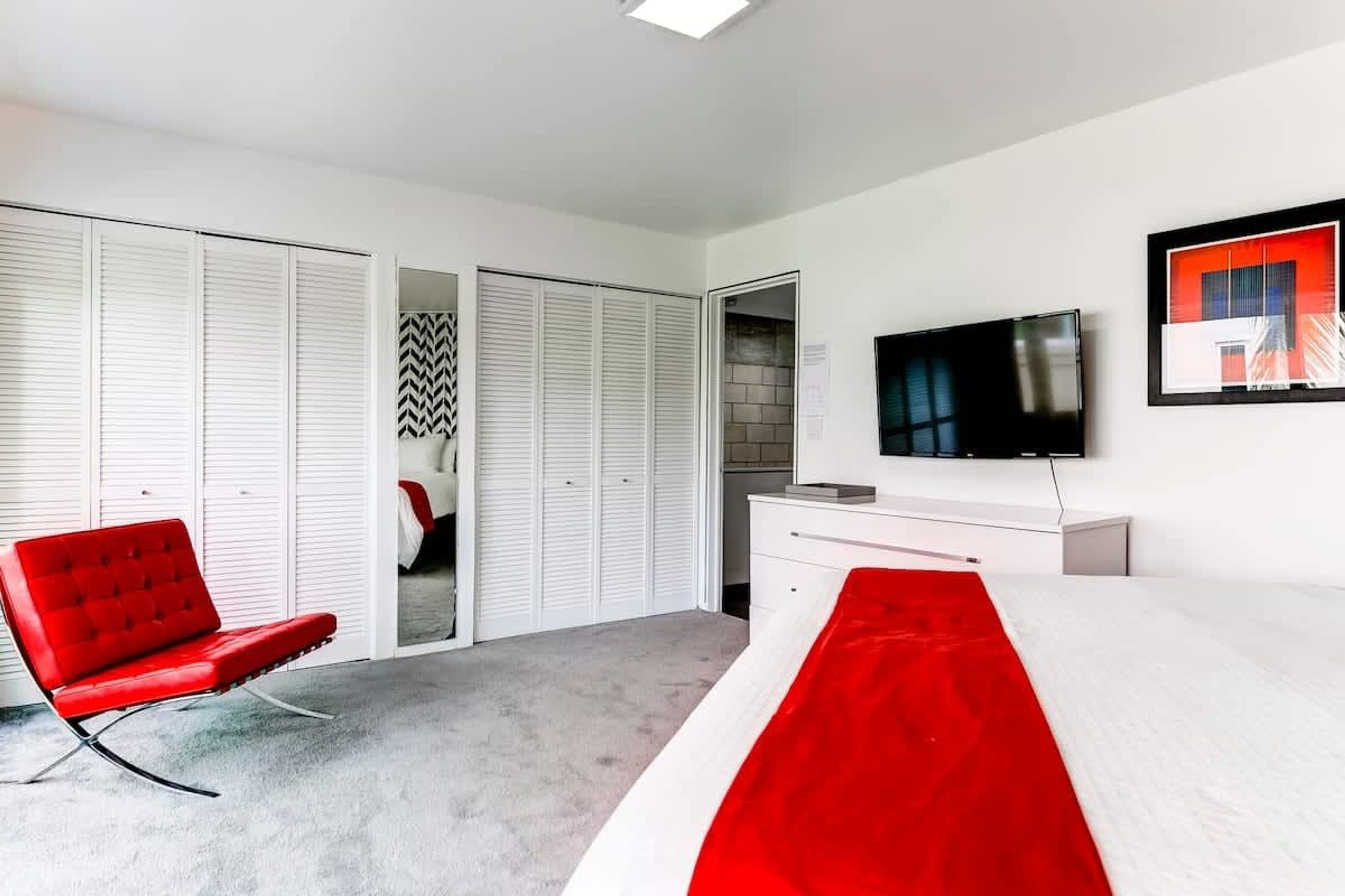 A modern hotel room with a bed, a red chair, a TV, and a wardrobe.