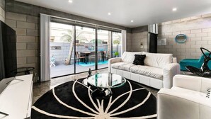 A modern living room with a white sofa, a glass coffee table, and a view of an outdoor patio with a pool. - Entire Townhouse Ft Lauderdale (Fort Lauderdale)