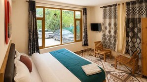 A bedroom with a bed, a TV, a chair, and a window with curtains. - The Nature Crest Manali (Manali)