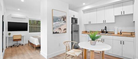 A modern kitchen with white cabinets, a dining table, and a large window overlooking a beach.