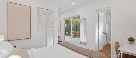 A modern bedroom with a large bed, a desk, and a view of an outdoor patio.