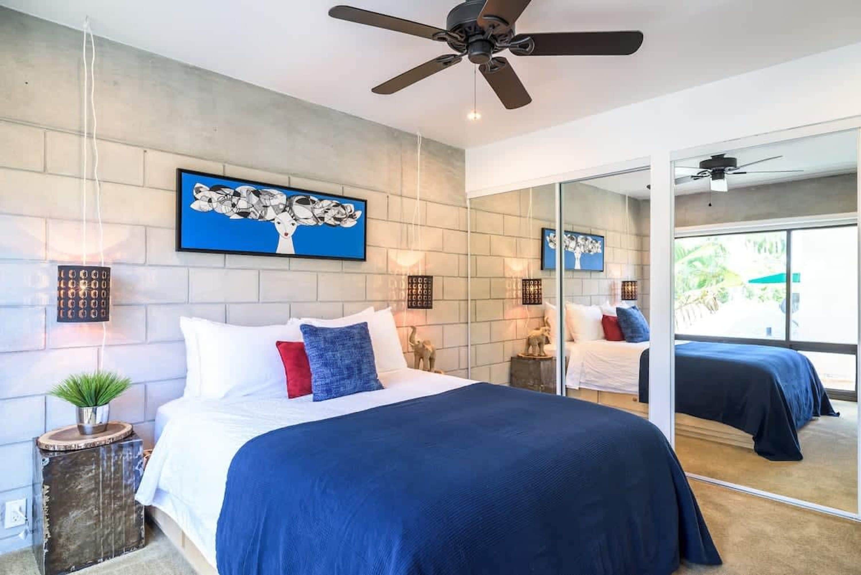 A modern bedroom with a large bed, a ceiling fan, and a large mirror reflecting the room.
