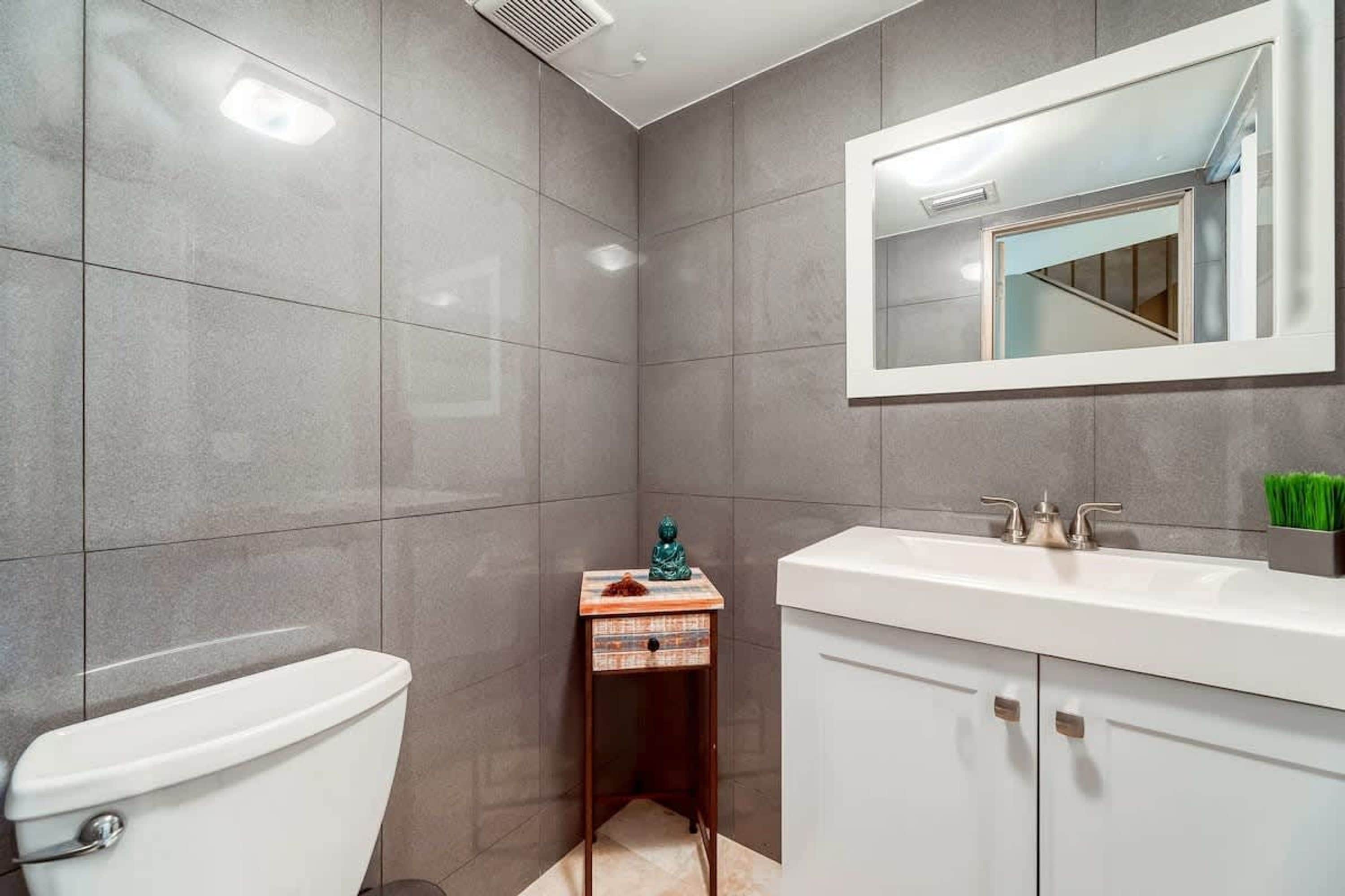 A bathroom with a toilet, a sink with a mirror, and a small cabinet.