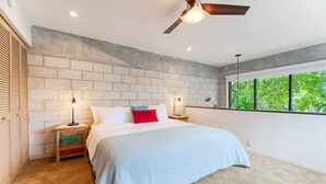 A bedroom with a large bed, a ceiling fan, and a window with a view of greenery. - Singer House on the Water (Fort Lauderdale)