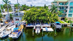 A marina with boats docked, surrounded by lush greenery and modern buildings. - Piano House on the Water (Fort Lauderdale)
