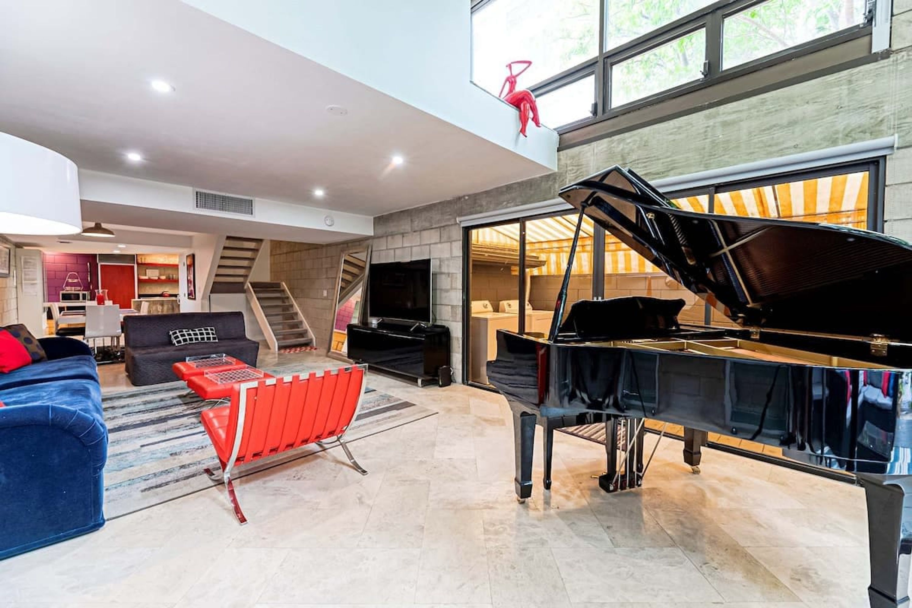 A spacious living room with a grand piano, a red chair, and a blue sofa.