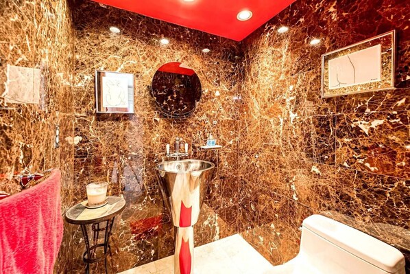 A bathroom with a marble wall, a sink, a toilet, and a mirror.