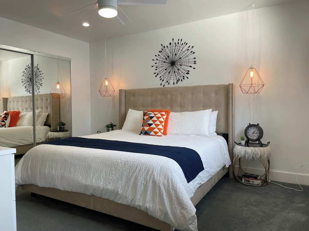 A modern bedroom with a large bed, a mirror, and two wall-mounted light fixtures.
