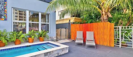 Un espace piscine avec une terrasse en bois, un palmier et une clôture.