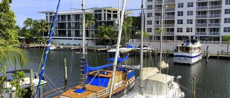A marina with several sailboats docked, a modern building with balconies, and a clear sky.