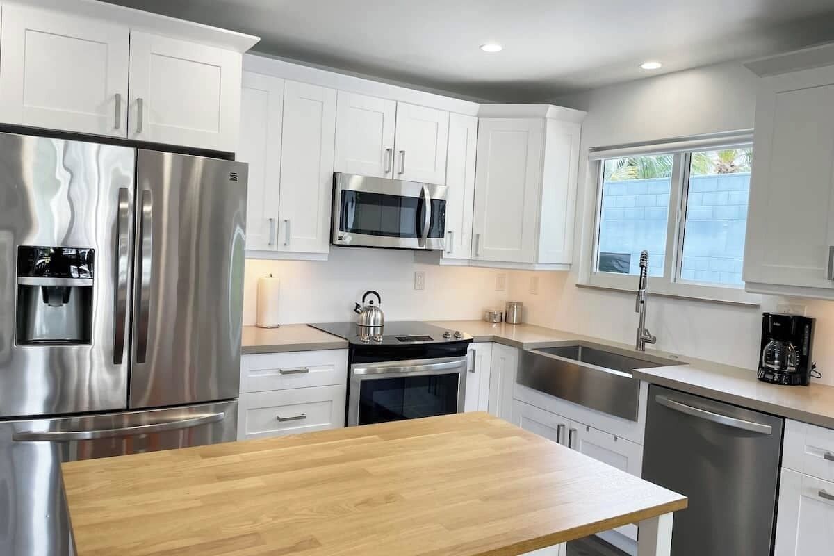A modern kitchen with white cabinets, stainless steel appliances, and a wooden countertop.